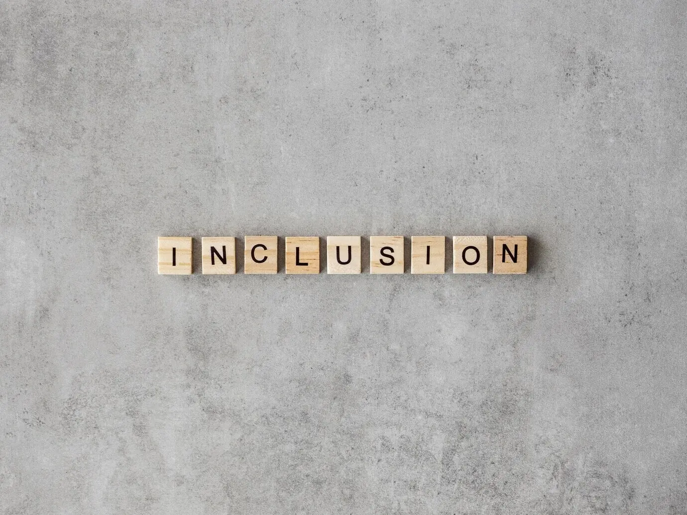 На мраморном фоне — слово «Inclusion», выложенное буквами Scrabble.